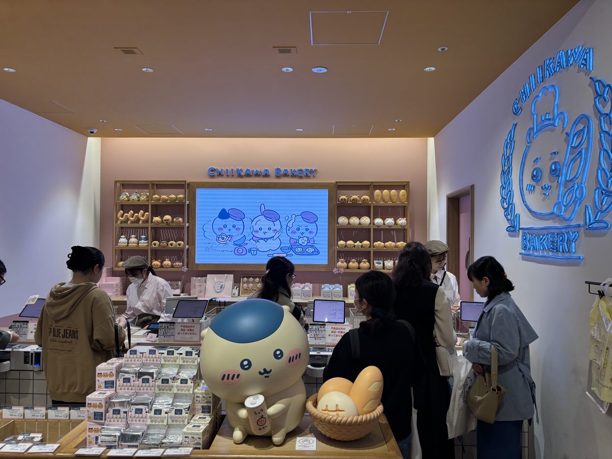 Inside Chiikawa Bakery Harajuku showing the main counter with character-shaped breads, a large Chiikawa plush figure, and visitors browsing the display